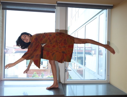 Woman in a rust-colored garment balancing beside tall windows