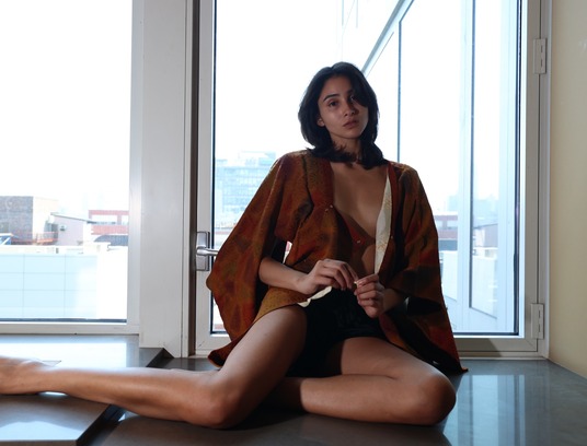 Woman in a rust-colored garment seated beside a window
